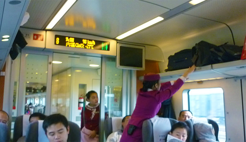 An attendant tidying the luggage rack on a D train