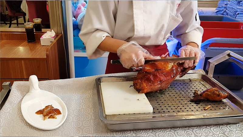 The cook cuts off the skin of the roast duck first